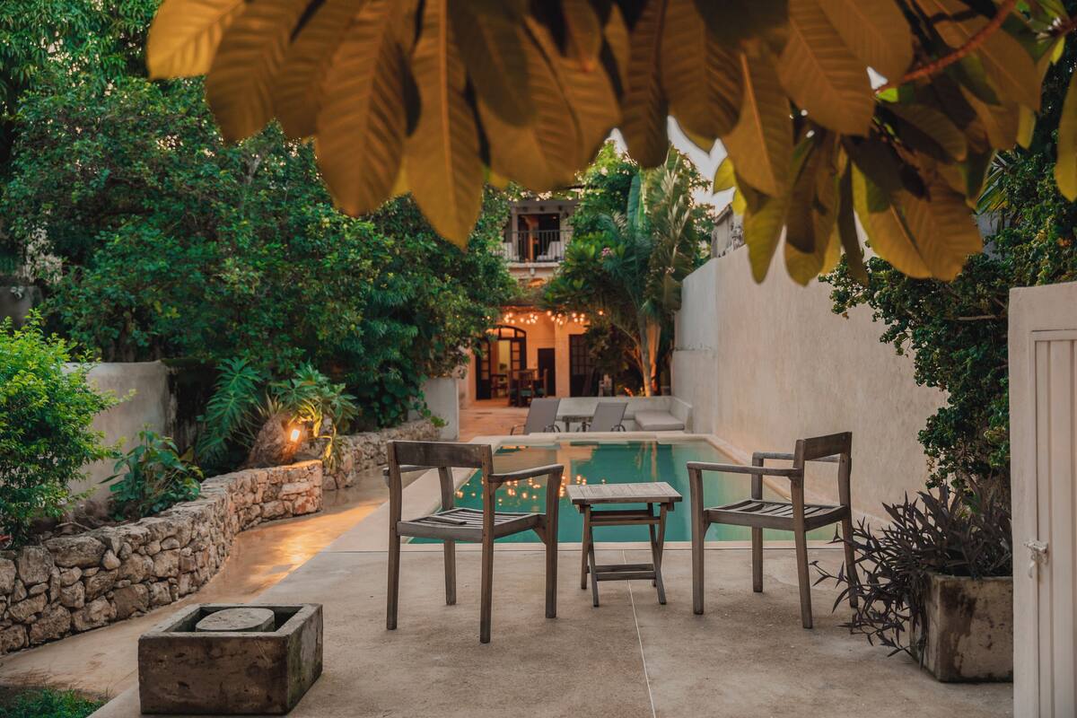 A pool area with a stone wall, wooden chairs, and a table.
