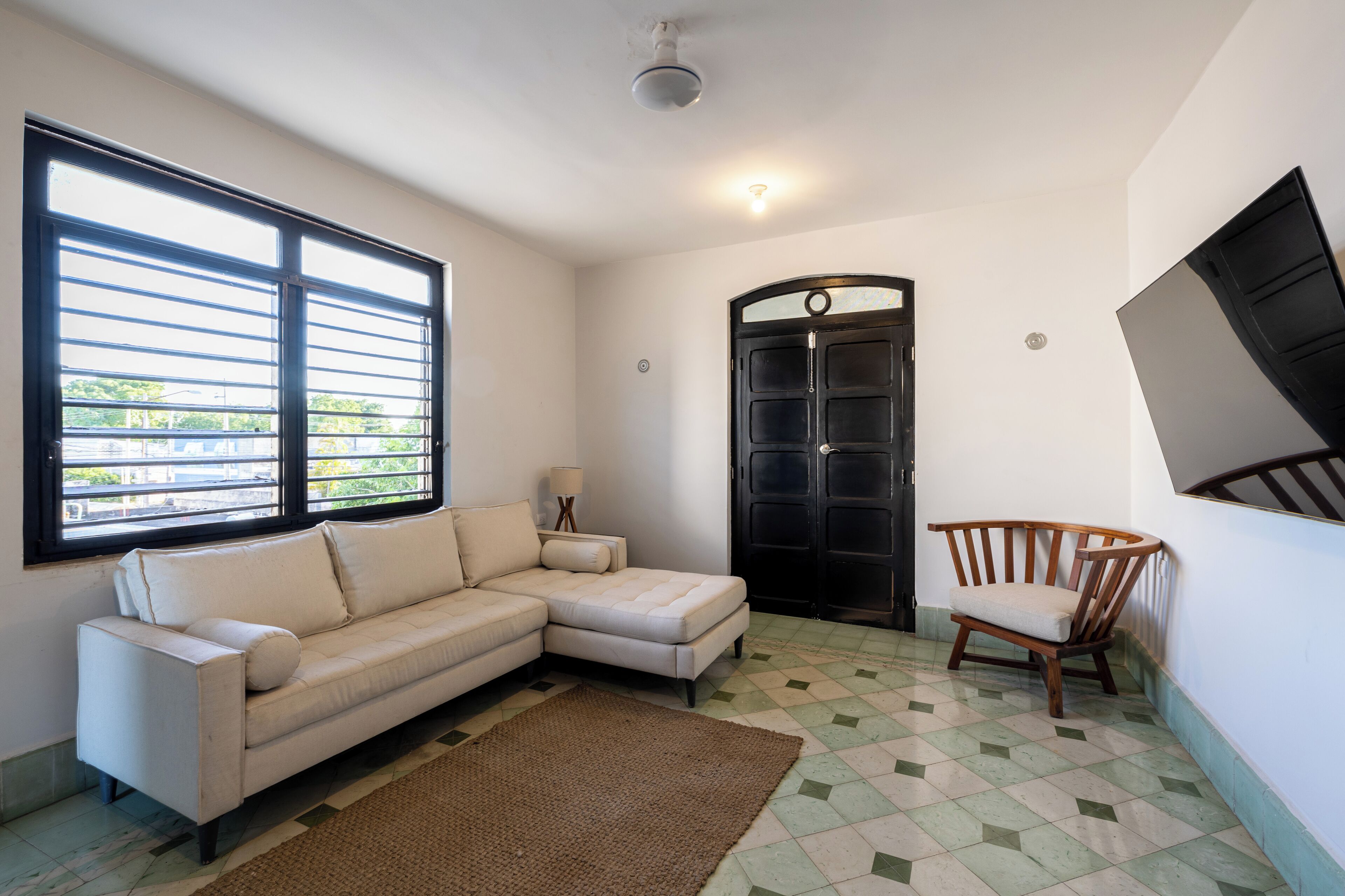 A living room with a sectional sofa, a wooden chair, a black door, and a window with blinds.