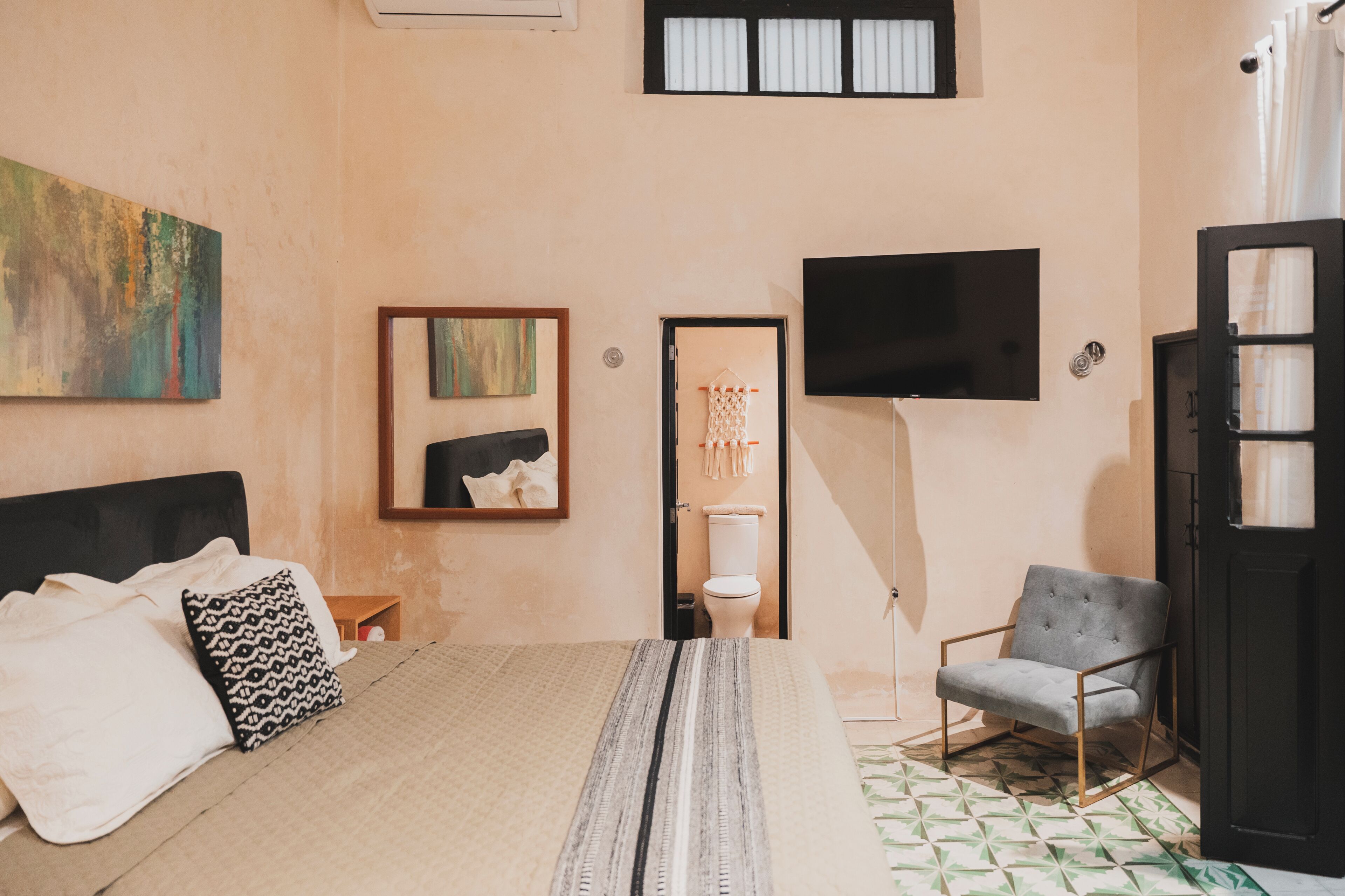 A bedroom with a bed, a chair, a TV, and a toilet.
