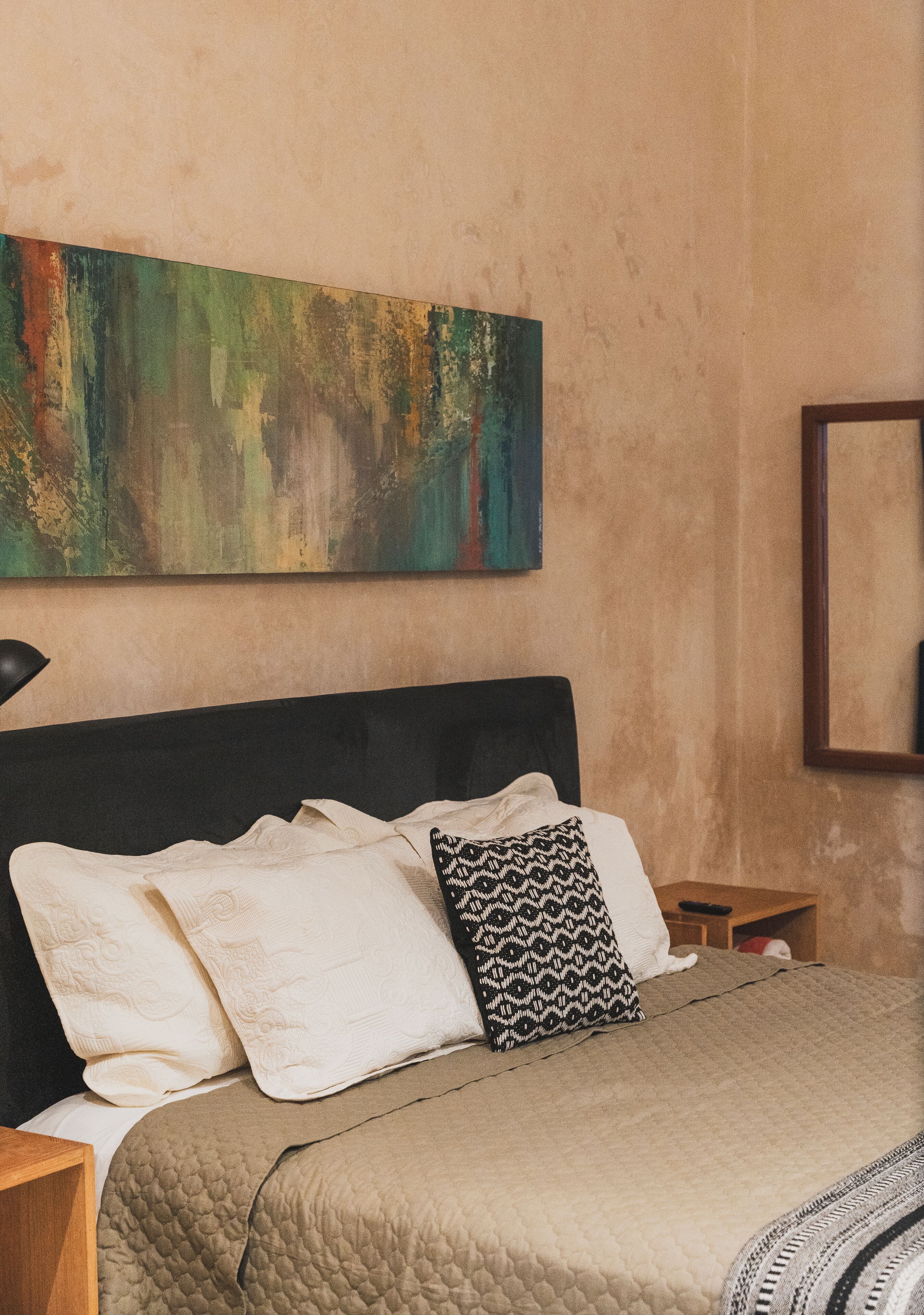 Une chambre à coucher avec un lit, des oreillers, une table de chevet, une lampe et un tableau au mur.