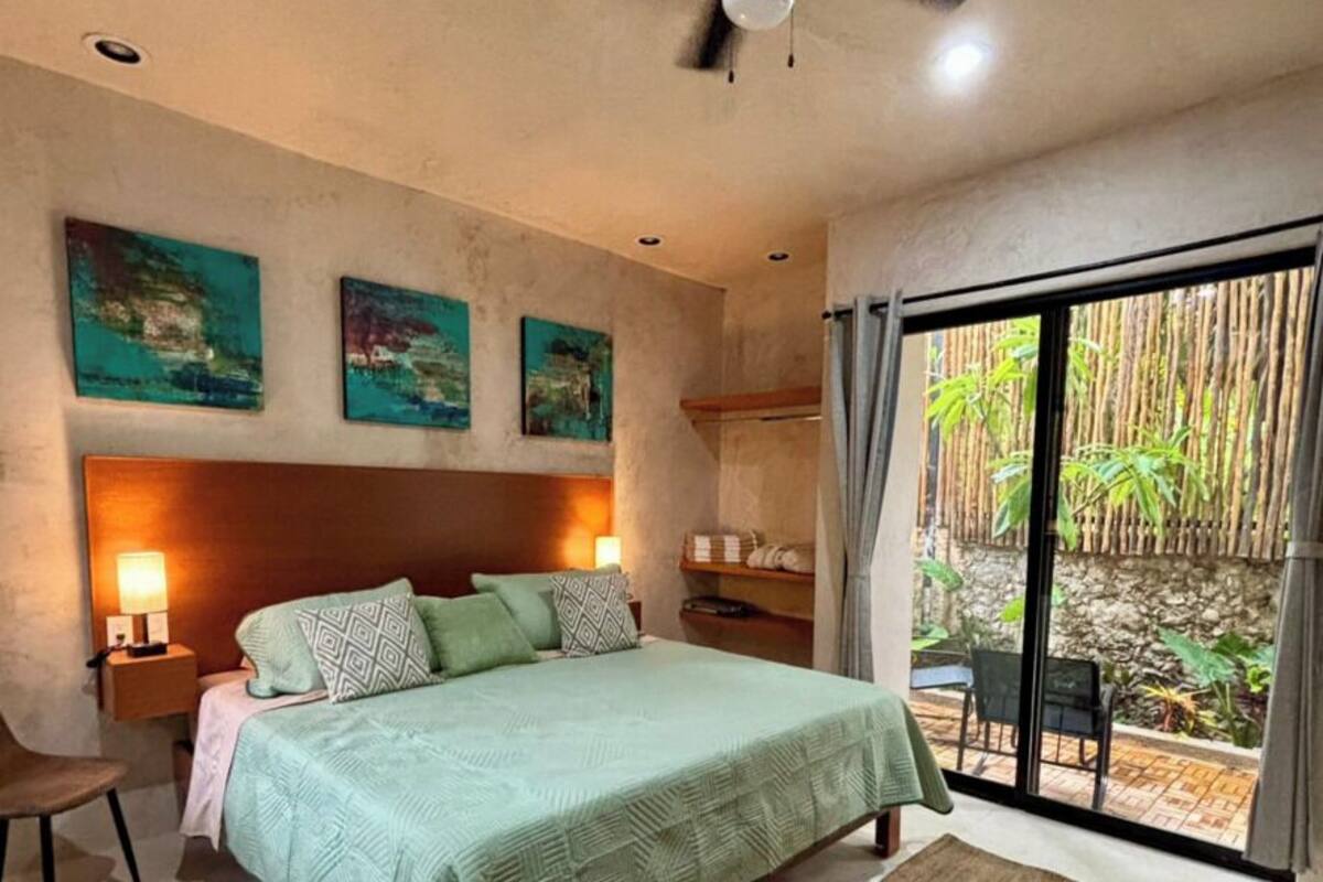 A bedroom with a bed, a ceiling fan, a nightstand, a chair, and a view of the outdoors.