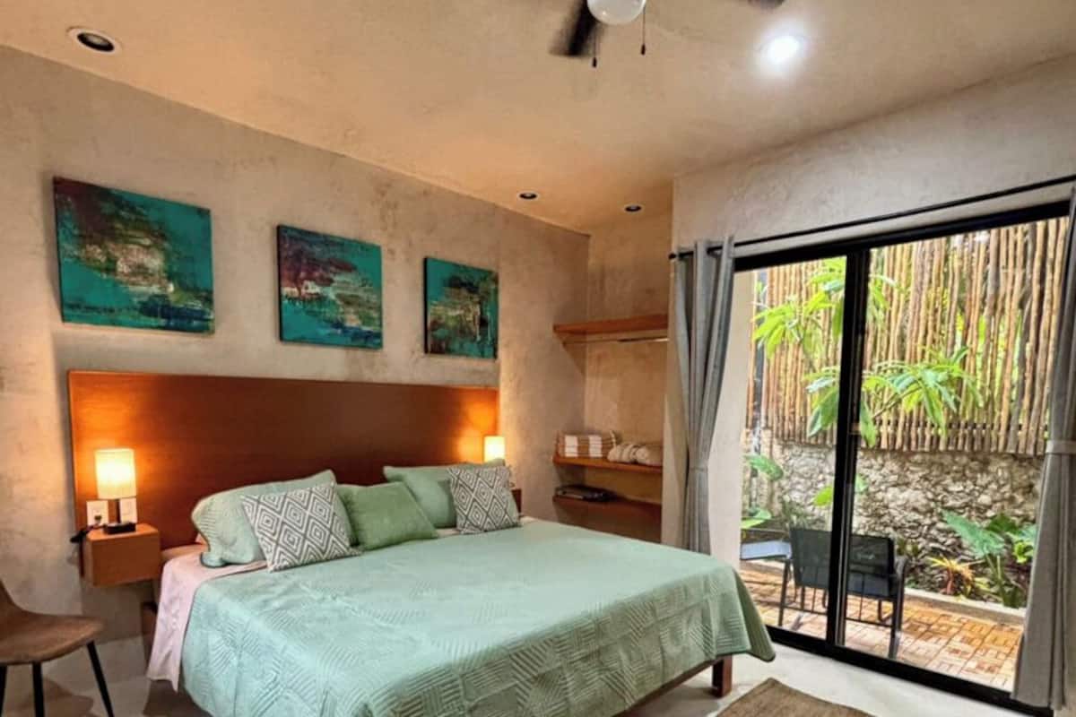 Un dormitorio con cama, ventilador de techo, mesita de noche, silla y vistas al exterior.