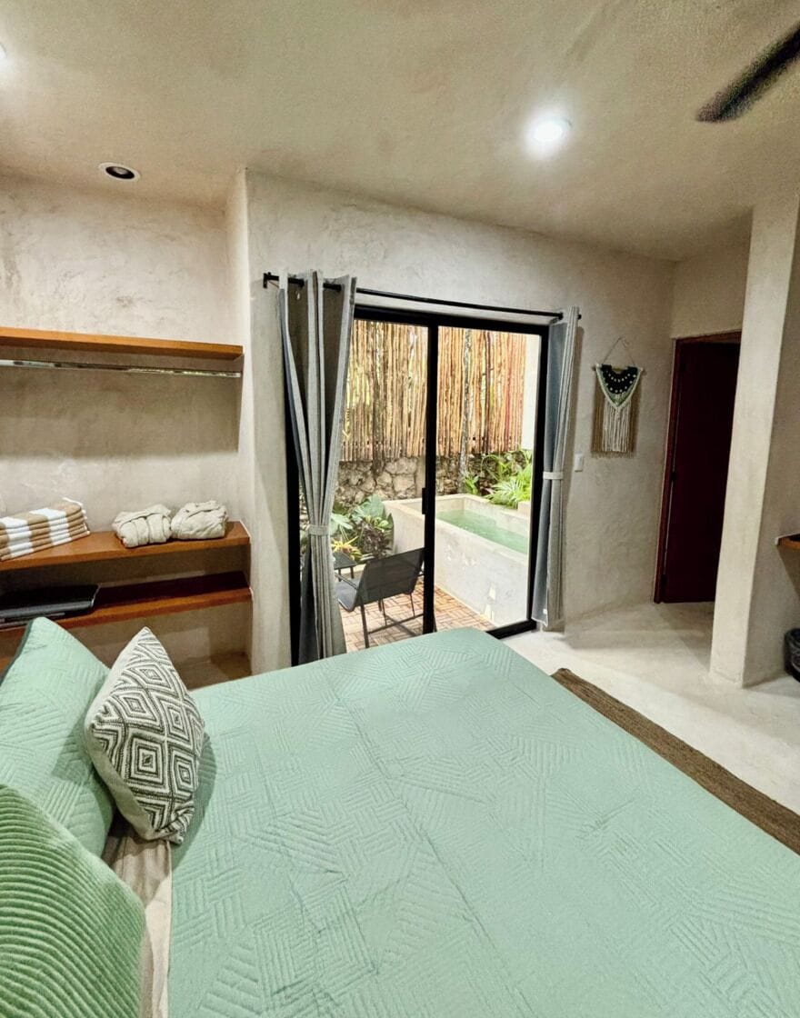 Een slaapkamer met een bed, een bank met handdoeken, een schuifdeur naar een balkon en een kleine tafel.