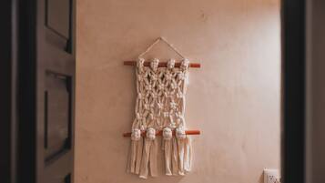 Un tapiz de macramé con una vara de madera y flecos, colgado en una pared lisa.