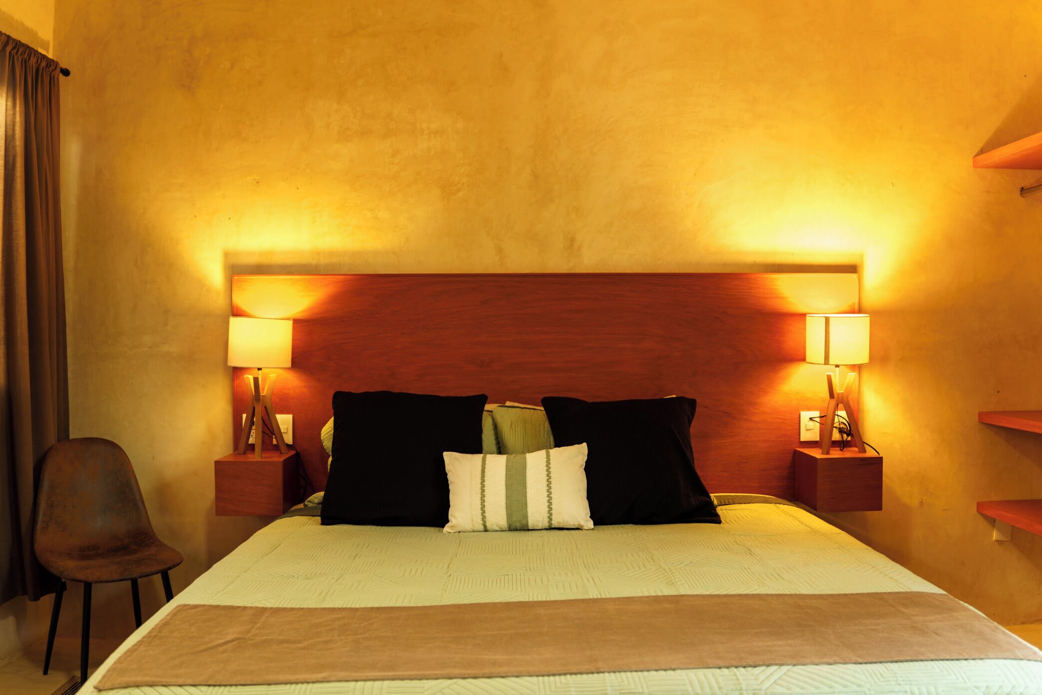 Une chambre d’hôtel avec un grand lit, deux tables de chevet avec des lampes, une chaise et une tête de lit en bois.
