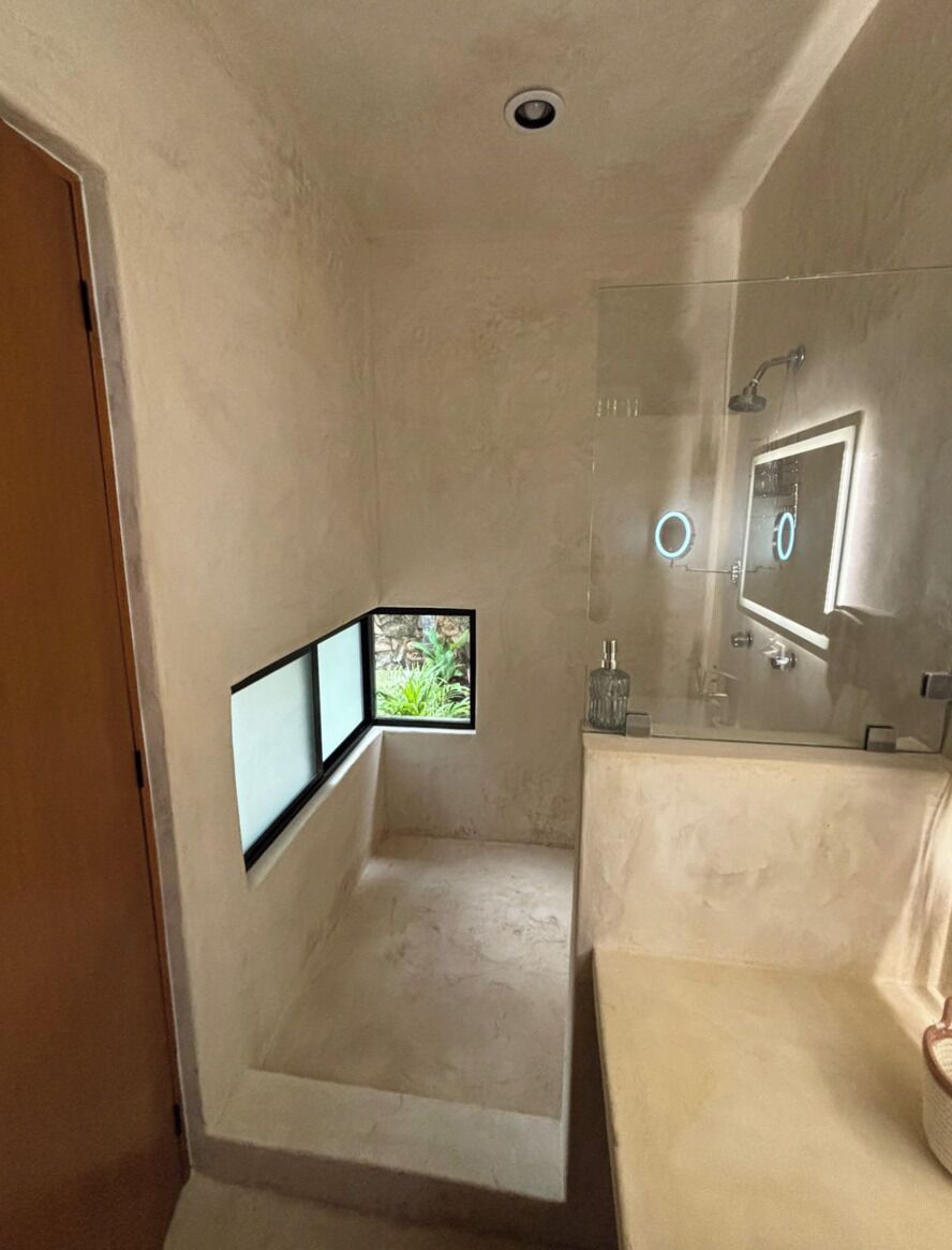 A bathroom with a glass shower enclosure, a mirror, and a window.