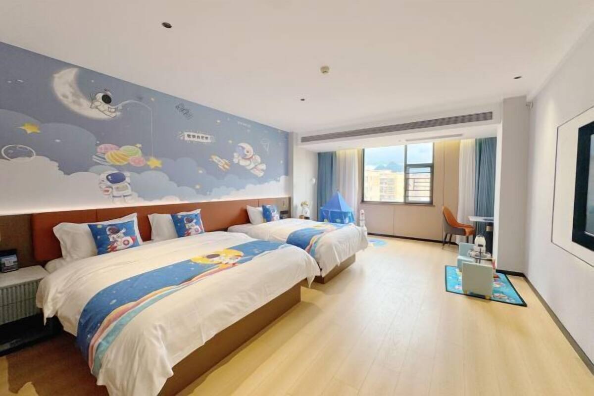 A hotel room with two beds, a large wall mural, a window with curtains, and a desk with a chair.