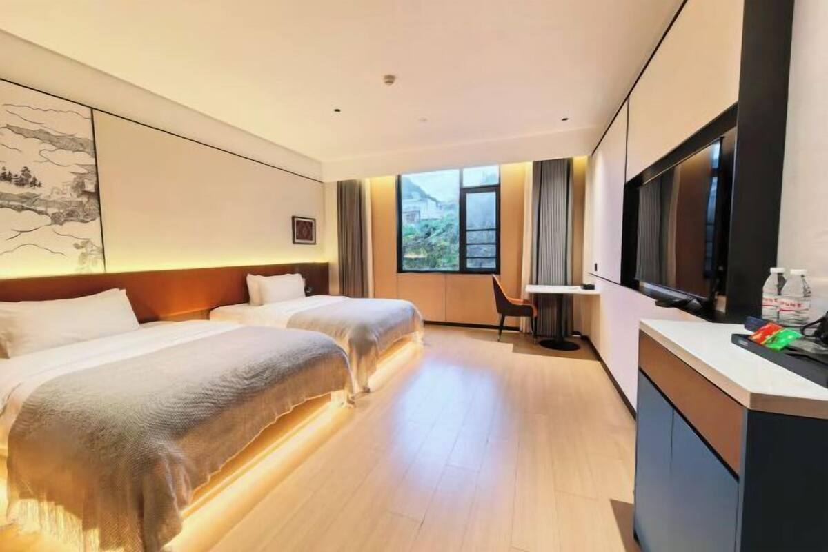 A hotel room with two beds, a desk, a chair, a TV, and a window with a view.