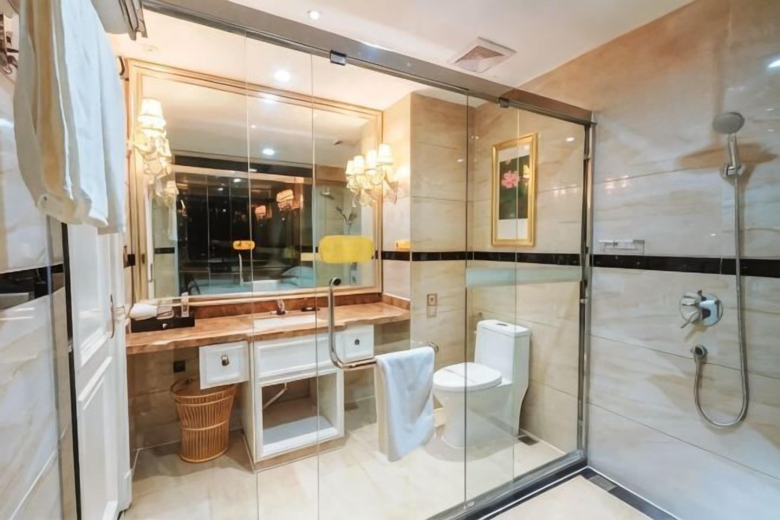 A modern bathroom with a glass shower enclosure, a marble-tiled wall, a large mirror, and a white toilet.