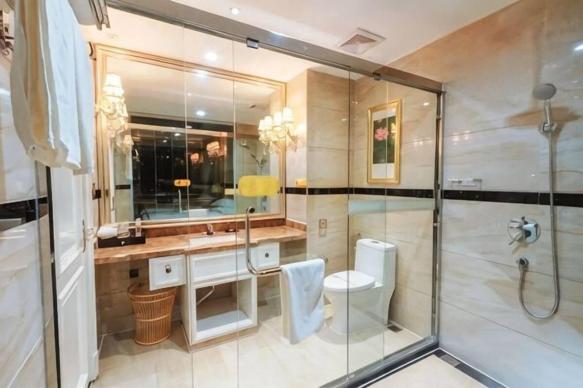 A modern bathroom with a glass shower enclosure, a marble-tiled wall, a large mirror, and a white toilet.