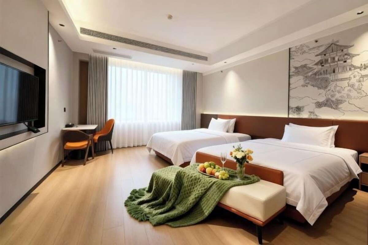 Habitación de hotel con dos camas, un escritorio, una silla y un televisor.