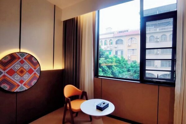 Una habitación de hotel con un ventanal grande, un adorno circular en la pared, una silla individual y una mesita.