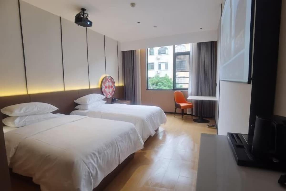 Ein Hotelzimmer mit zwei Betten, einem Schreibtisch, einem Stuhl, einem Fernseher und einem Fenster mit Vorhängen.