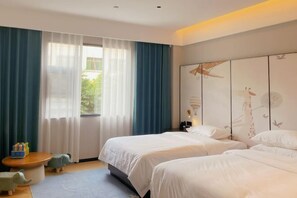 Habitación de hotel con dos camas, un ventanal con cortinas translúcidas, una mesita con juguetes y una pared con un mural de aves.