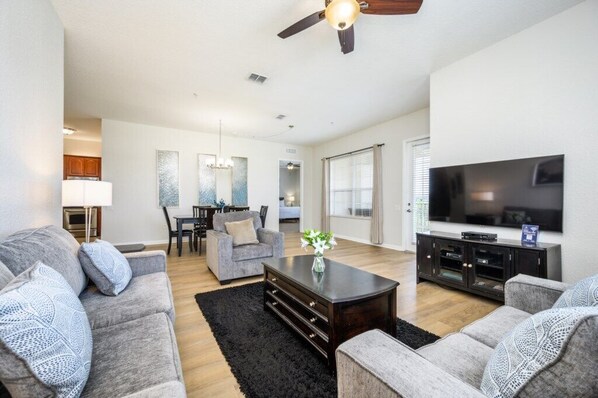 A modern living room with a ceiling fan, a flat-screen TV, and a dining area with a chandelier. - Epic Universe Penthouse Vacation Condo, Near the Parks - 2014 (Orlando)