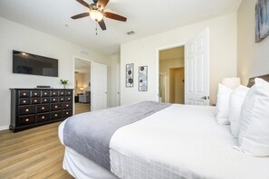 A bedroom with a large bed, a ceiling fan, a dresser, and artwork on the walls. - Epic Universe Penthouse Vacation Condo, Near the Parks - 2014 (Orlando)