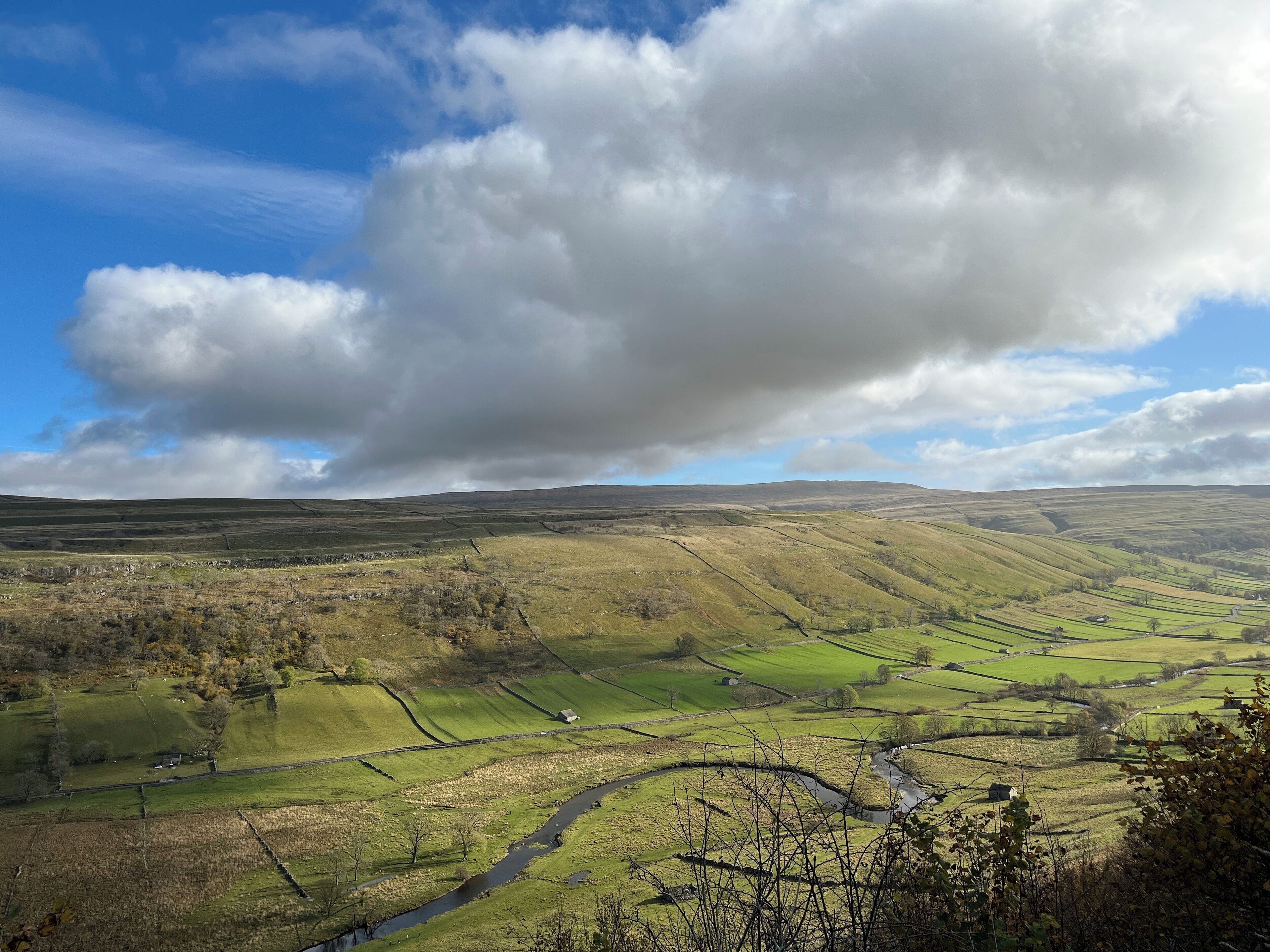 A panoramic view of a rural landscape with rolling hills, a river, and scattered houses.