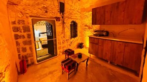 A cozy room with a stone wall, wooden cabinets, a small table with a chair, and a bed with a window. - Edo Evleri (Mardin)