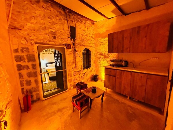 A cozy room with a stone wall, wooden cabinets, a small table with a chair, and a bed with a window. - Edo Evleri (Mardin)