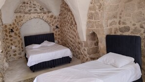 A bedroom with a stone wall and an arched ceiling, featuring two beds with dark headboards. - Edo Evleri (Mardin)