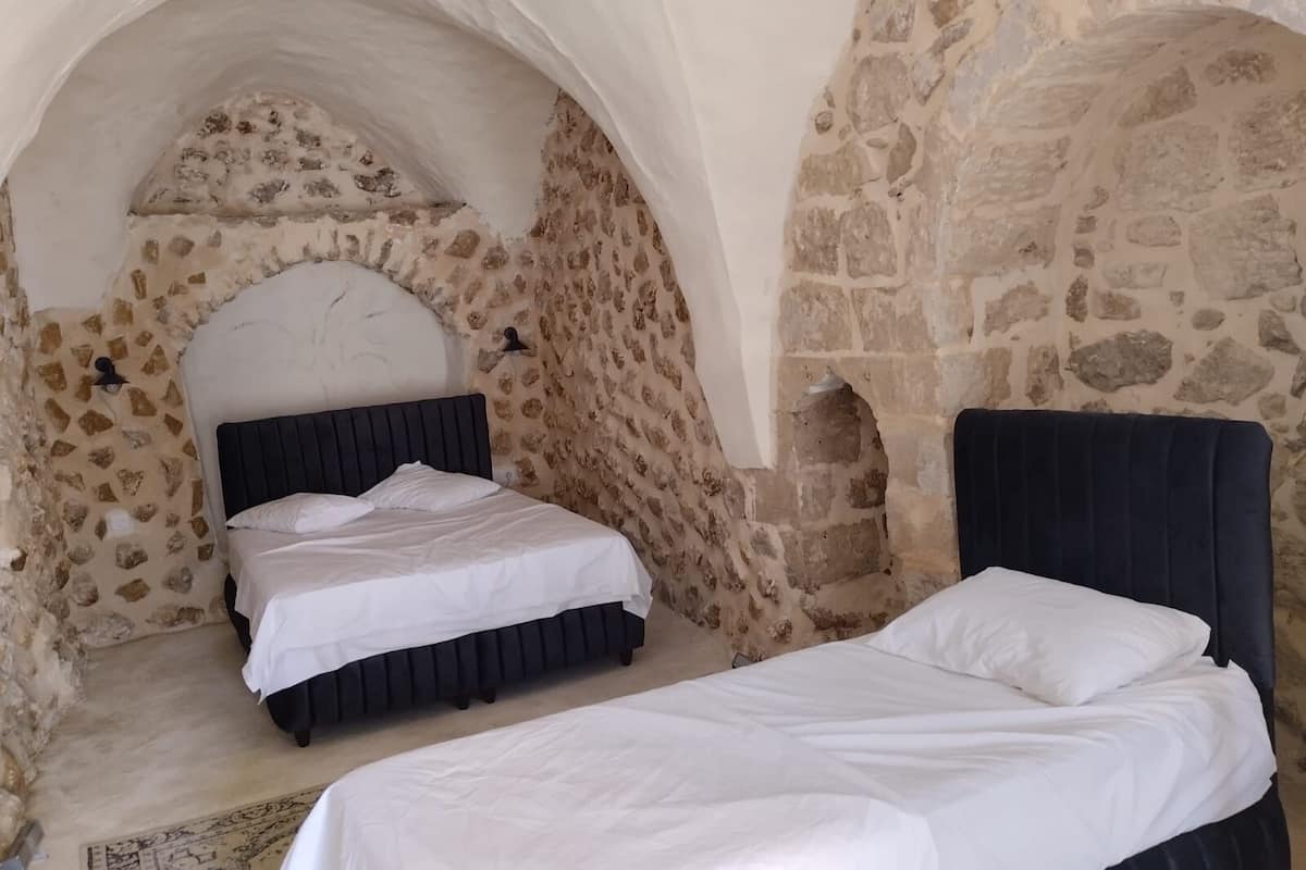 A bedroom with a stone wall and an arched ceiling, featuring two beds with dark headboards.