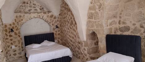 A bedroom with a stone wall and an arched ceiling, featuring two beds with dark headboards.