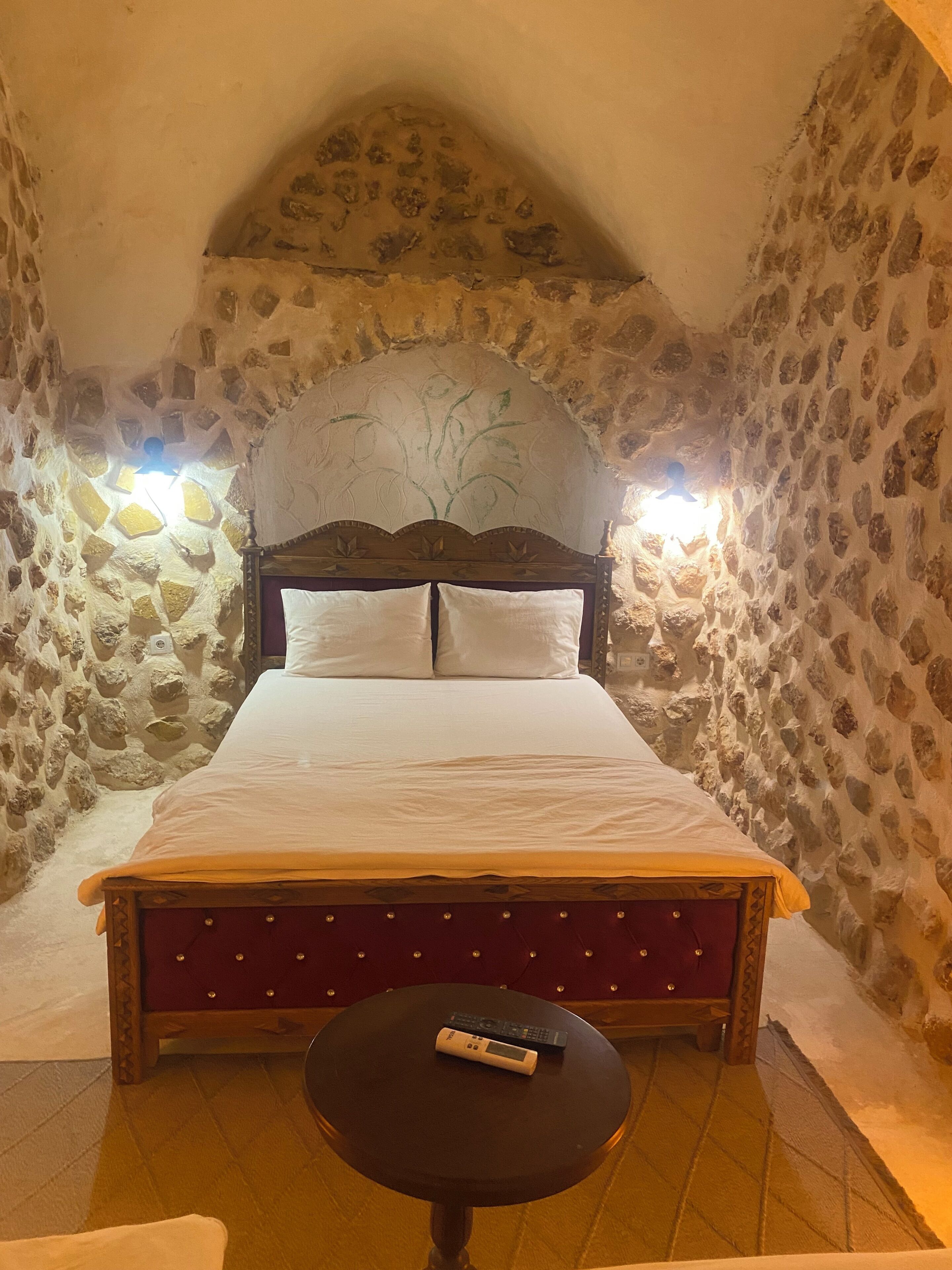 Ein Schlafzimmer mit Steinwänden, einem Bett, einem kleinen Tisch und einer Fernbedienung auf dem Tisch.