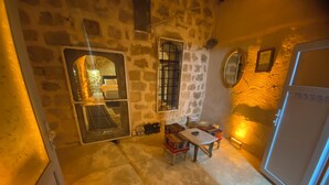 A stone-walled room with a table and chairs, a mirror, and a door. - Edo Evleri (Mardin)