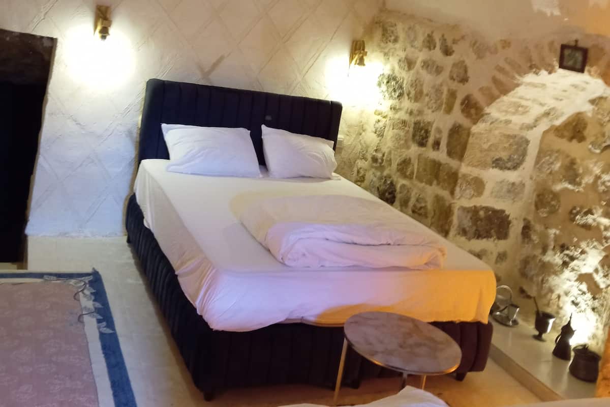 A cozy bedroom with a stone wall, a bed with white linens, and a small round table.