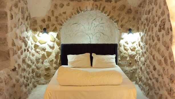 A bed in a stone-walled room with a vaulted ceiling and a tree mural above it. - Edo Evleri (Mardin)