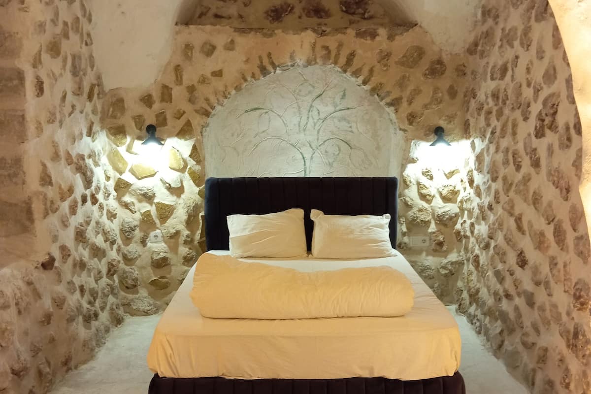 A bed in a stone-walled room with a vaulted ceiling and a tree mural above it.