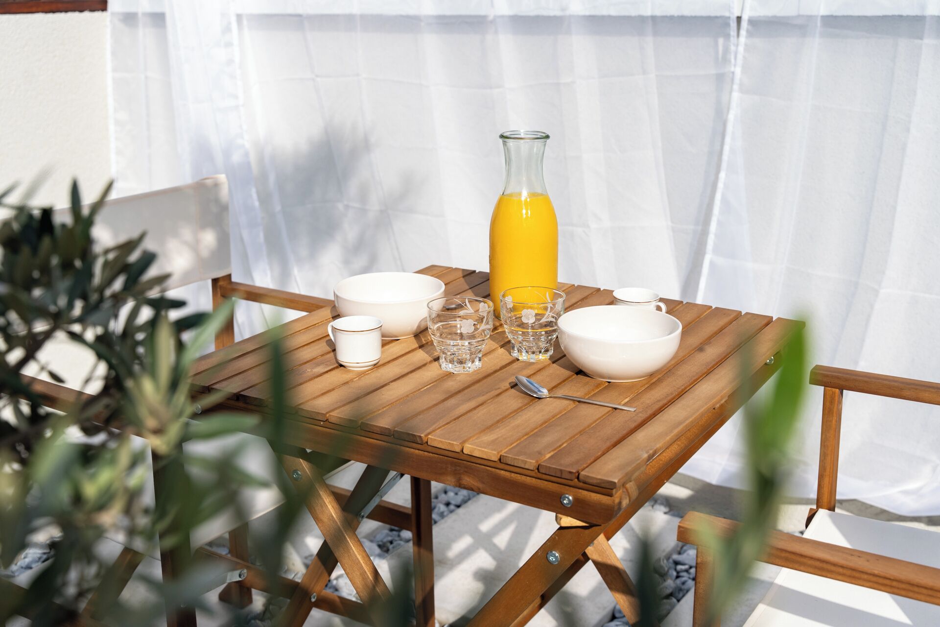 Une table en bois, dressée avec des bols blancs, des verres et une bouteille jaune, qui contient probablement une boisson.