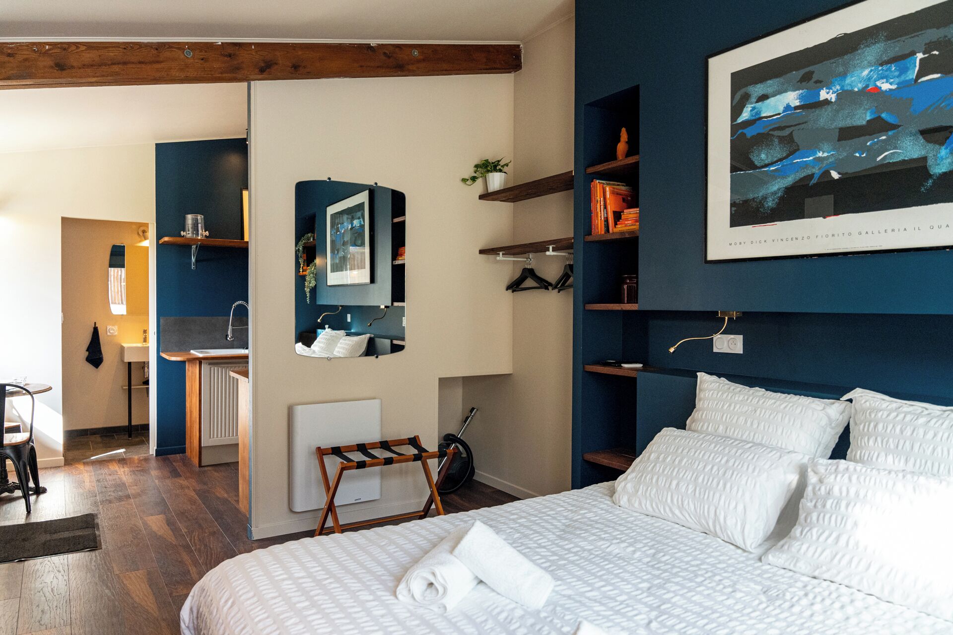Une chambre à coucher avec un lit, un miroir, une étagère remplie de livres et un tableau accroché au mur.