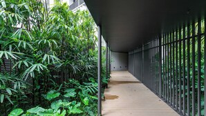 A covered walkway with a wooden floor, surrounded by dense green foliage and metal railings. - Charlie Onze22 Vila Madalena (São Paulo)