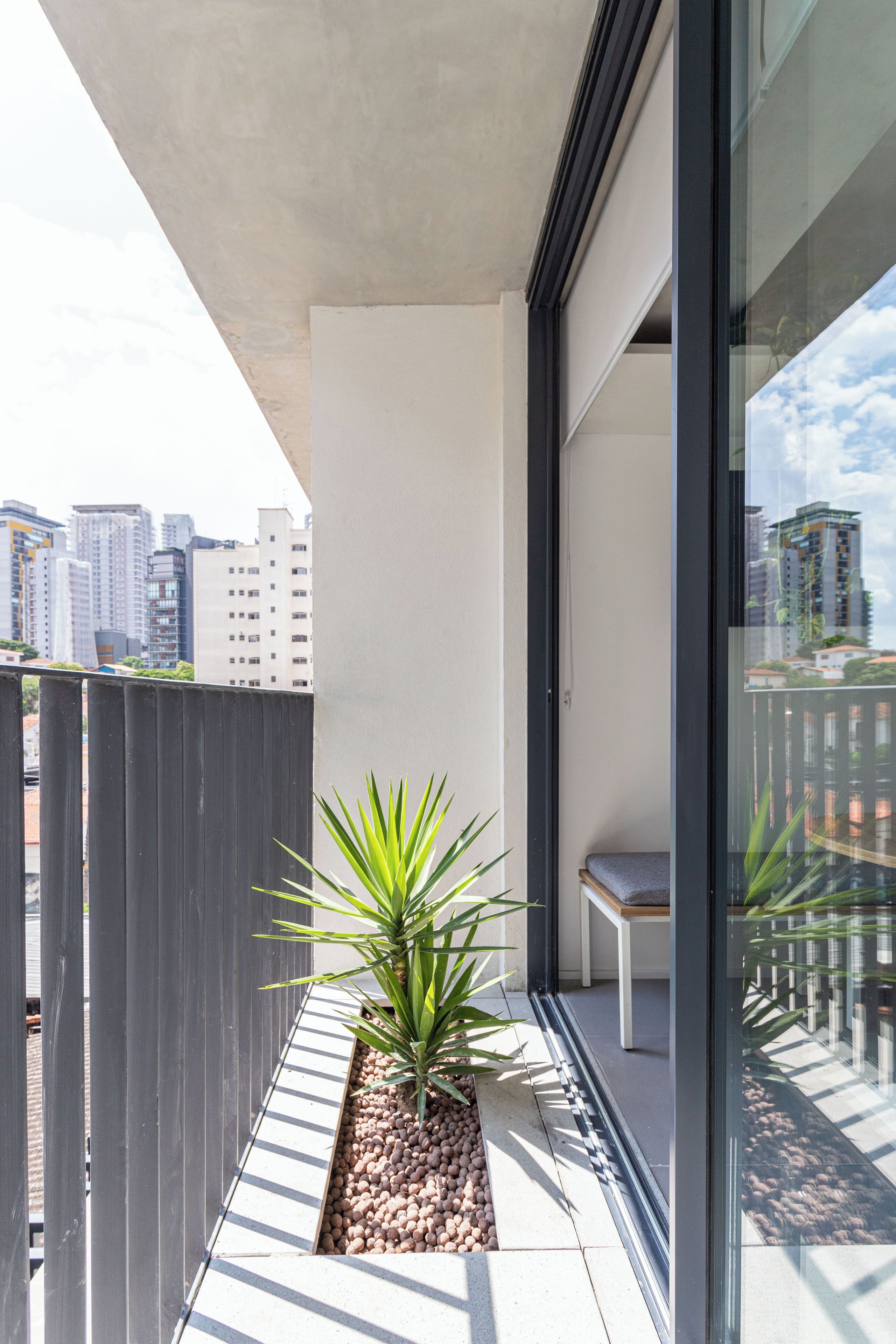 A balcony with a potted plant, a bench, and a city view.