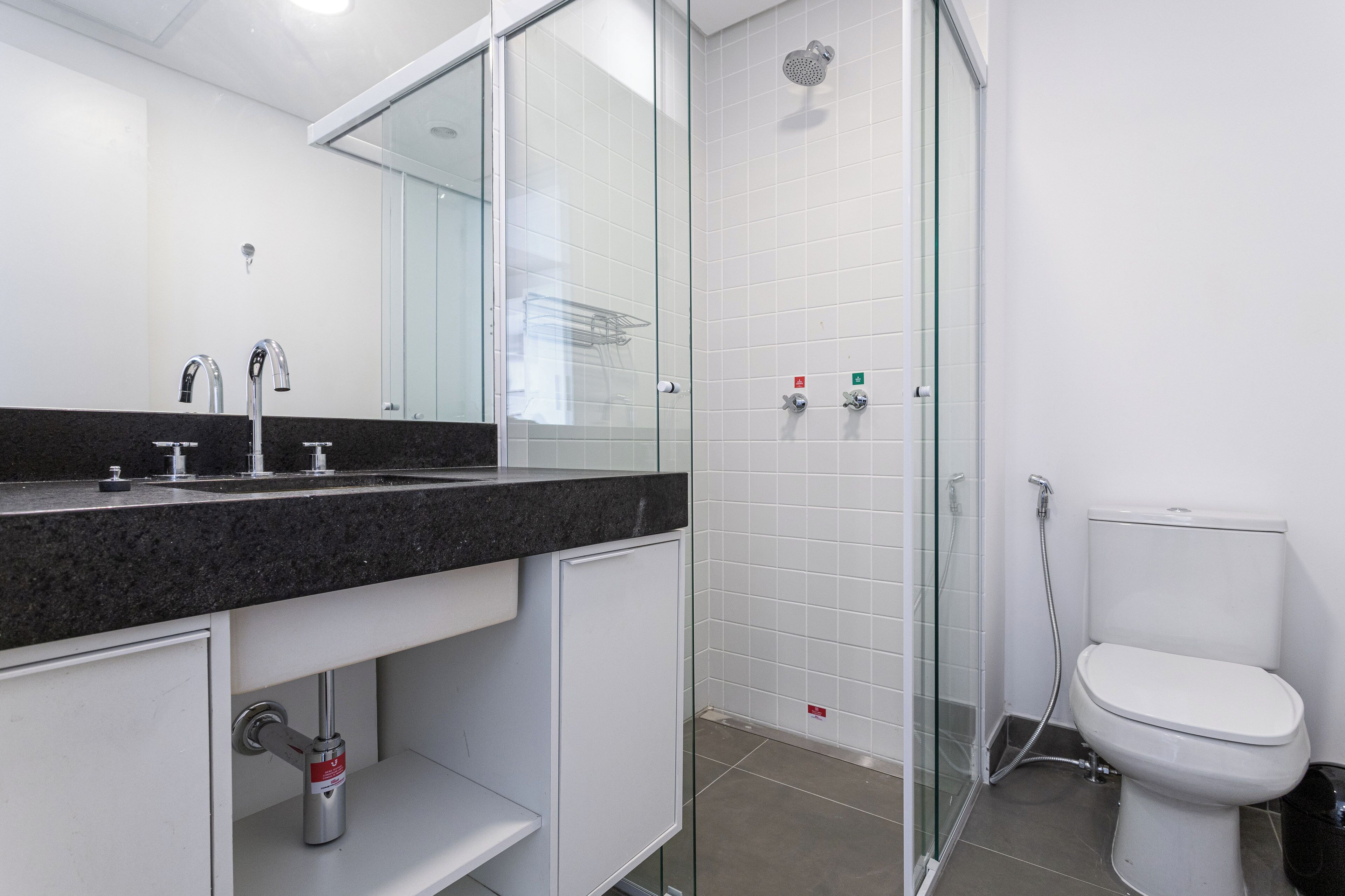 A modern bathroom with a glass-enclosed shower, a white toilet, and a granite countertop with a mirror.