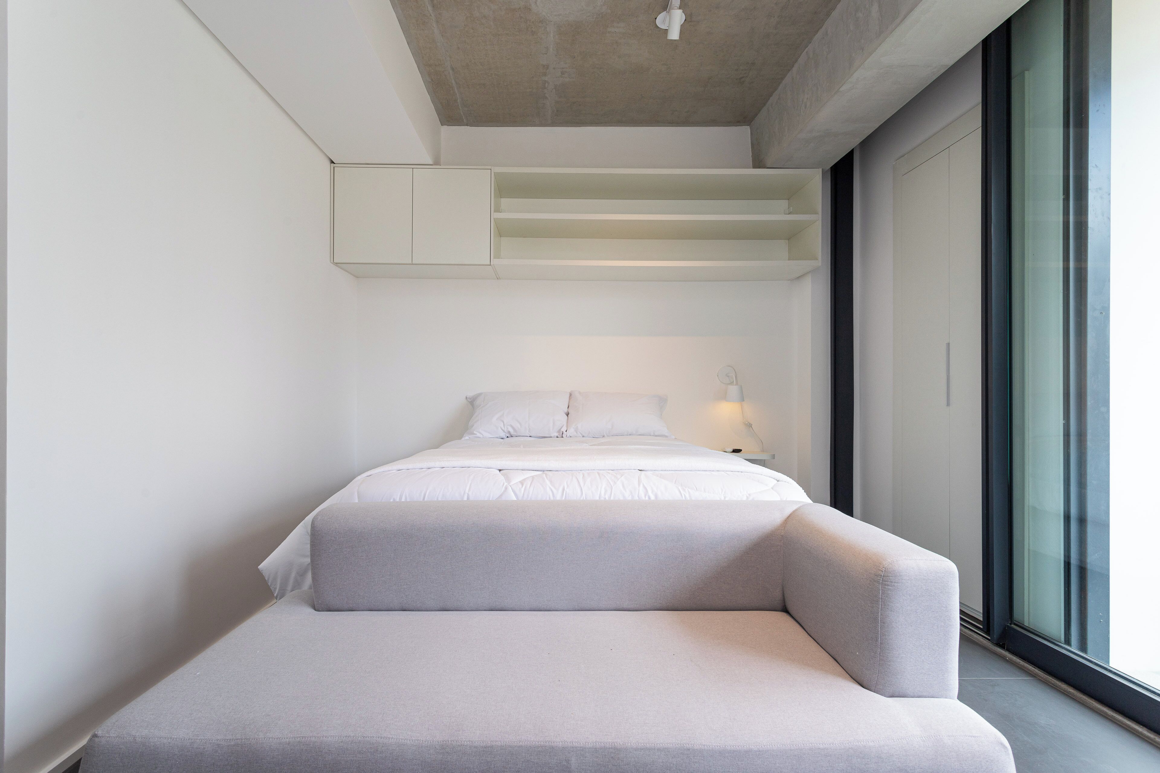 A modern bedroom with a bed, a built-in bench, and a large window.