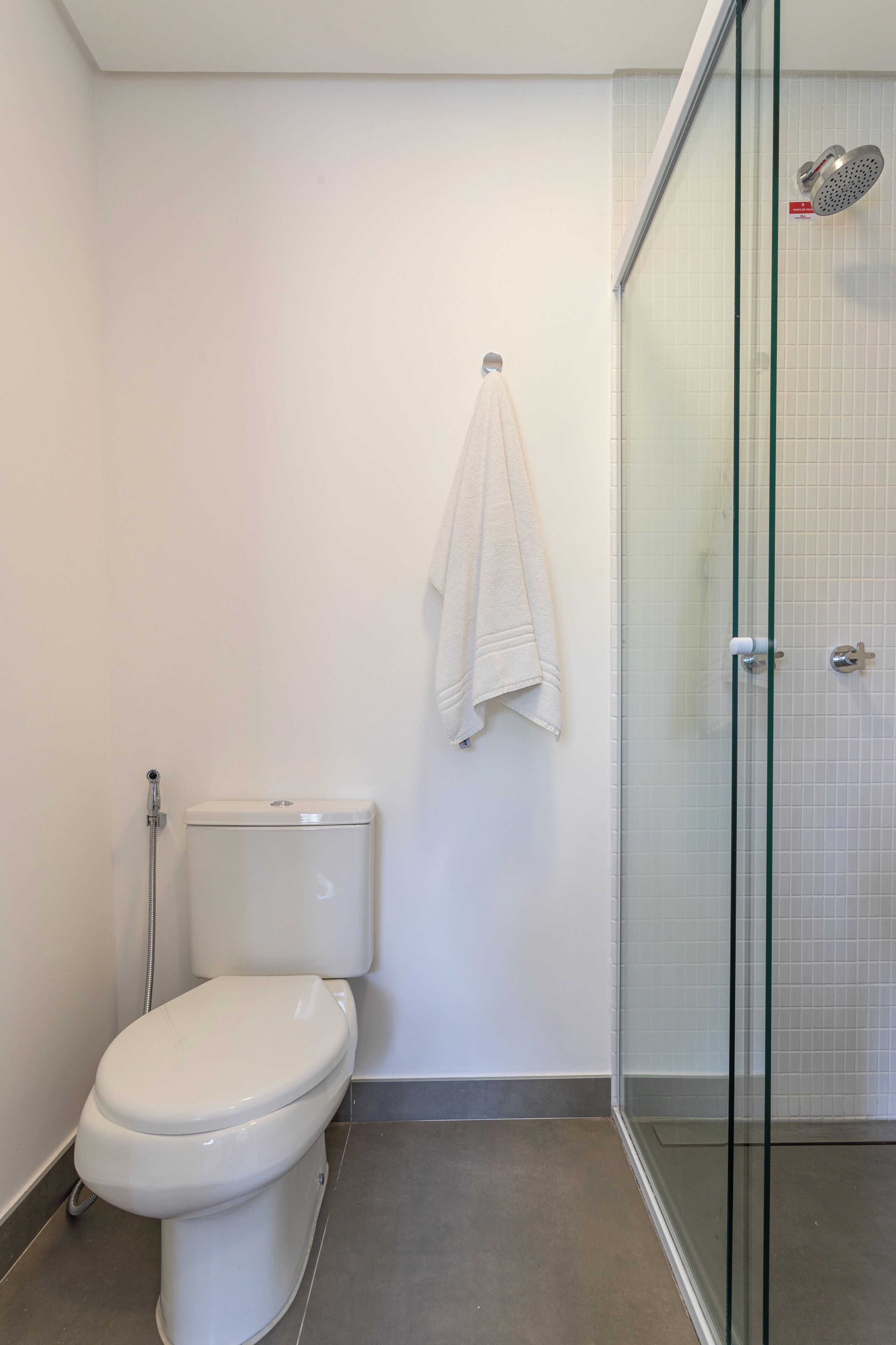 Een badkamer met een toilet, een glazen douchecabine en een witte handdoek aan de muur.