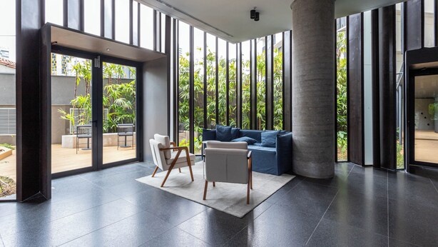 A modern interior with a large window, a blue sofa, a white chair, and a concrete pillar. - Charlie Onze22 Vila Madalena (São Paulo)