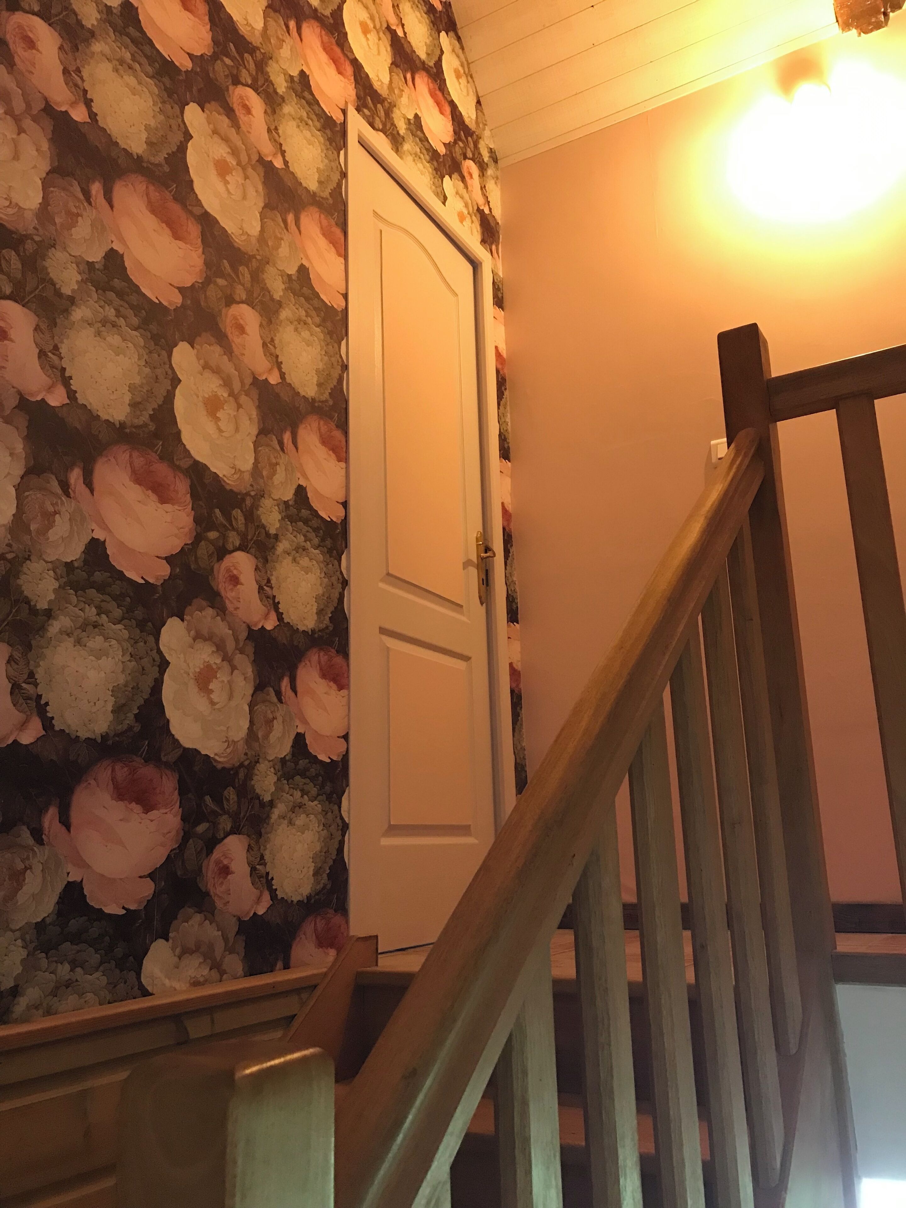 A staircase with wooden handrails leading to a door with a floral wallpaper design.