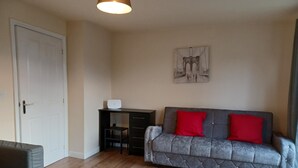 Una sala de estar con un sofá gris, cojines rojos, un escritorio pequeño y una puerta.