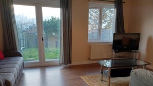 Una sala de estar con un sofá, una mesa de centro de cristal, un televisor y una puerta corrediza de vidrio que da a un patio trasero.