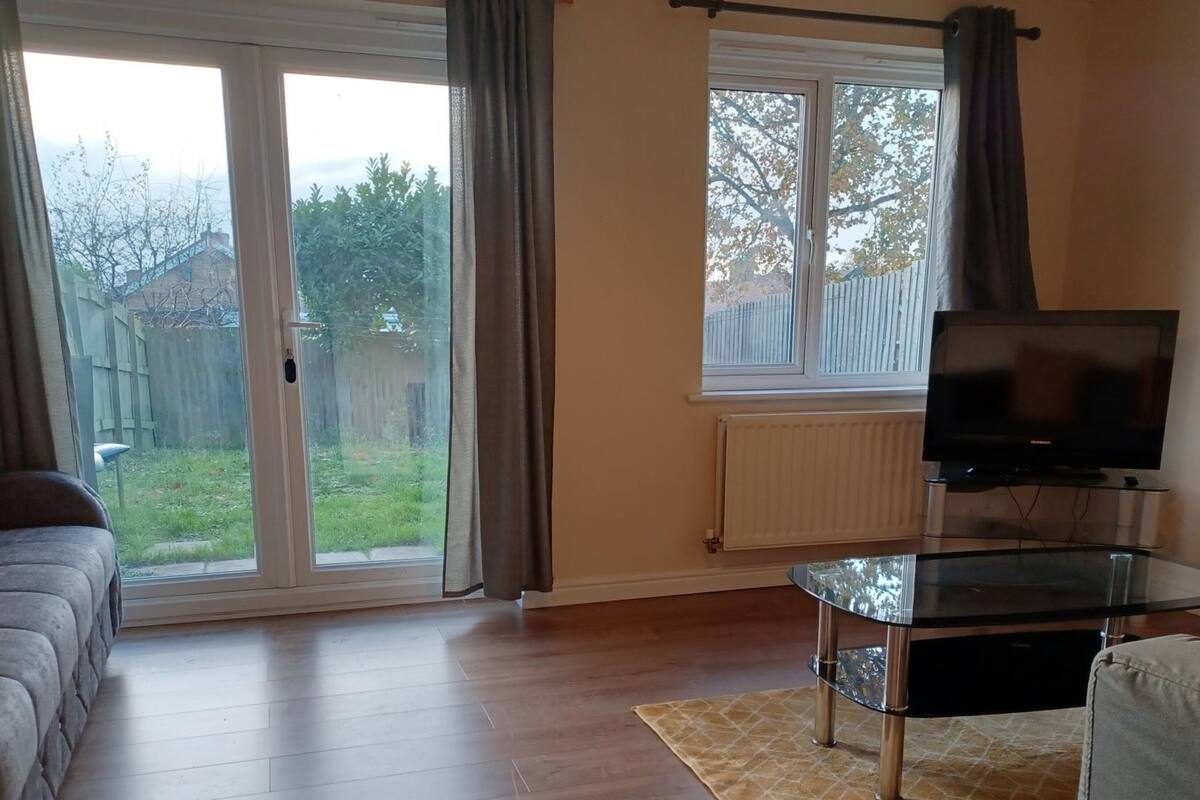 Een woonkamer met een bank, een glazen salontafel, een televisie en een schuifdeur die uitkomt op een achtertuin.