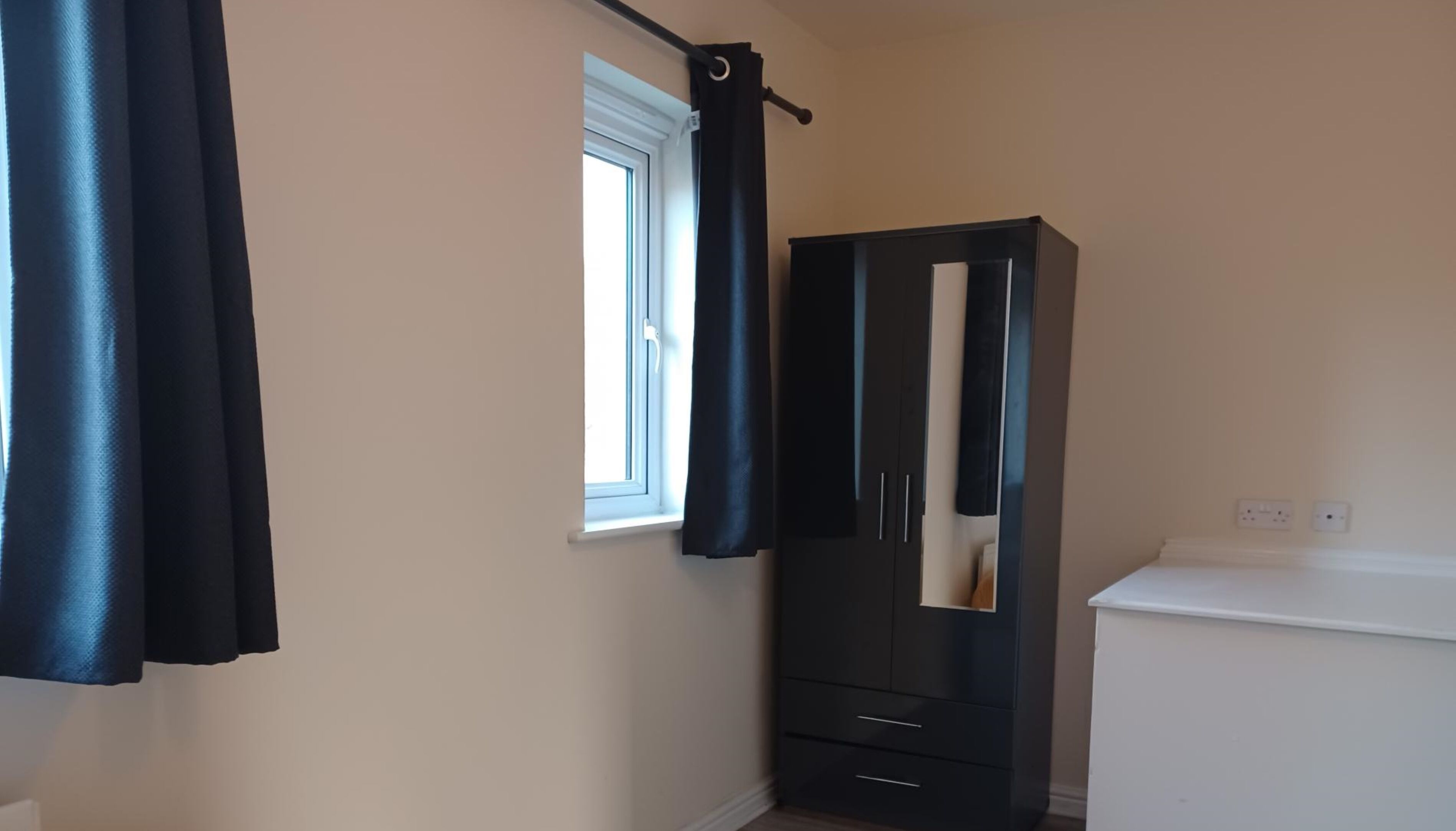A room with a window, a black wardrobe, and a white cabinet.