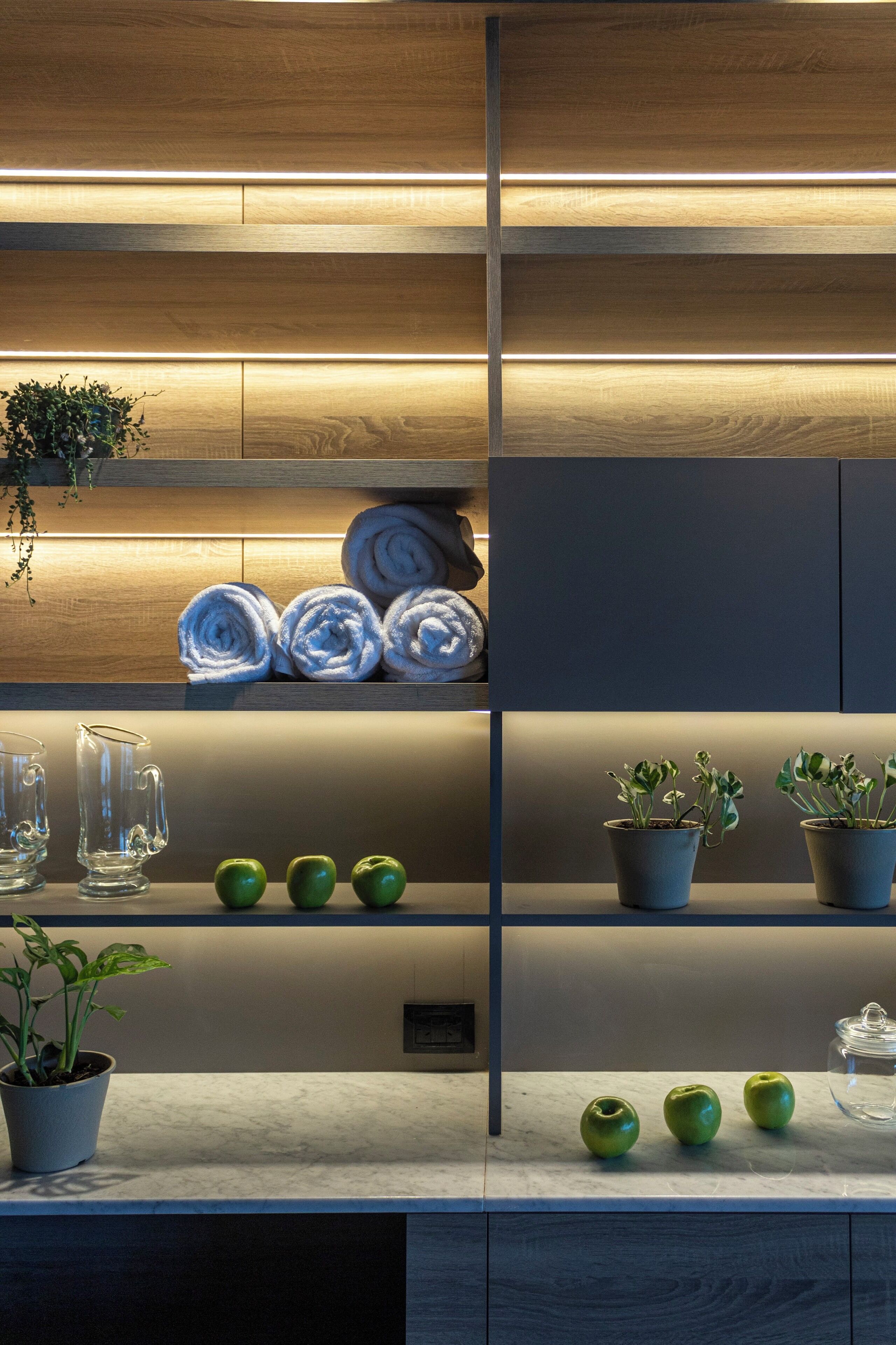 Una cocina moderna con armarios de madera, encimera de mármol, toallas ordenadas y plantas en macetas.