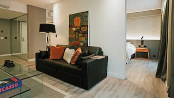 A modern living room with a black sofa, a glass coffee table, and a painting on the wall.