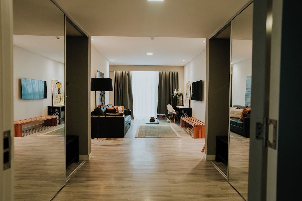 A modern hotel room with a wooden floor, a sofa, a coffee table, and a TV.