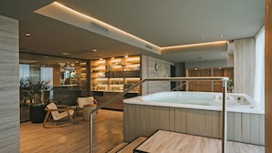 Et moderne spa-område med jacuzzi, trægulv og siddeplads med planter.