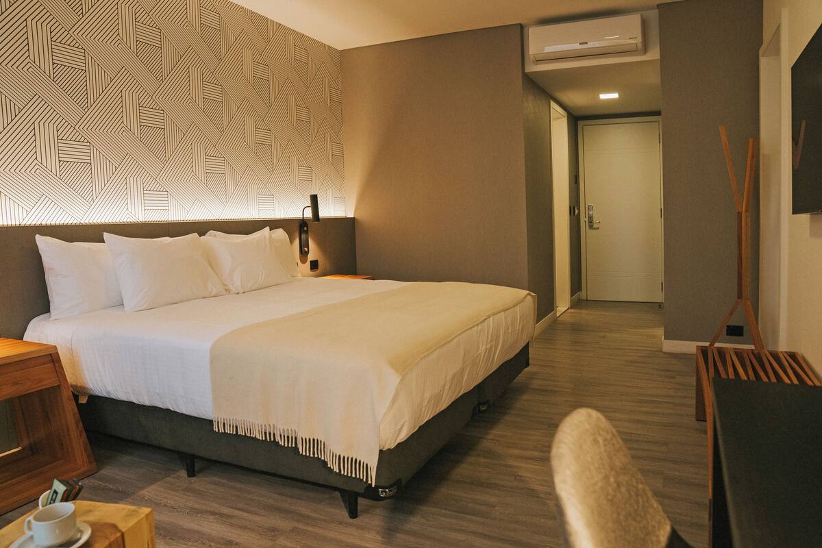 A hotel room with a large bed, a bedside table, a chair, and a desk.