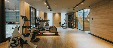 Un gimnasio con equipo de ejercicio, suelo de madera y ventanas amplias.
